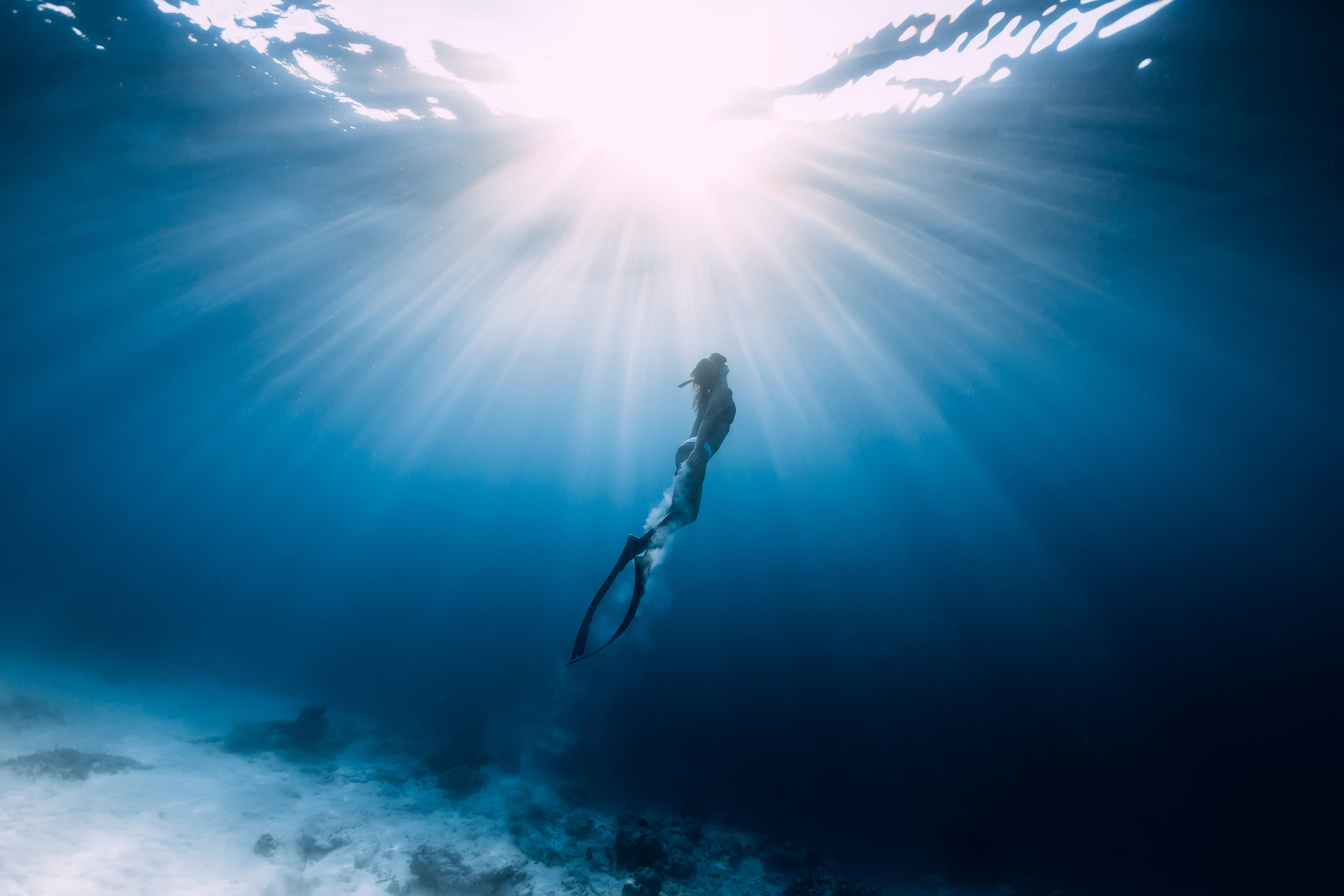 Woman freediver glides over sandy sea with fins