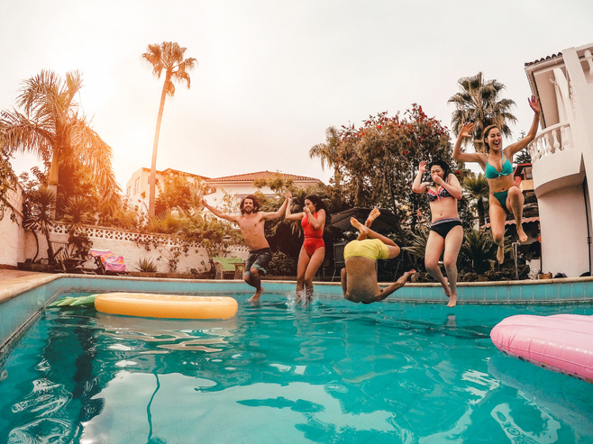 Group of Happy Friends Jumping in Pool at Sunset Time 